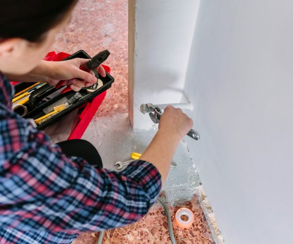 Female plumber tightening pipe with wrench in heating installation